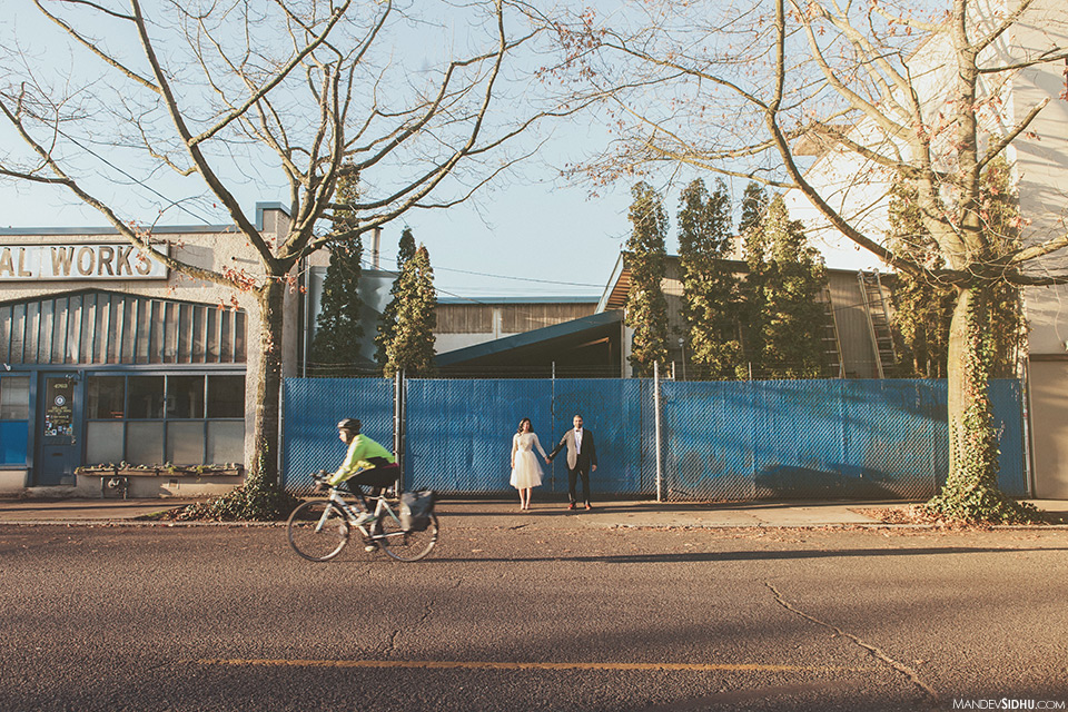 Couple stands in front of blue fence in downtown Ballard for engagement pics